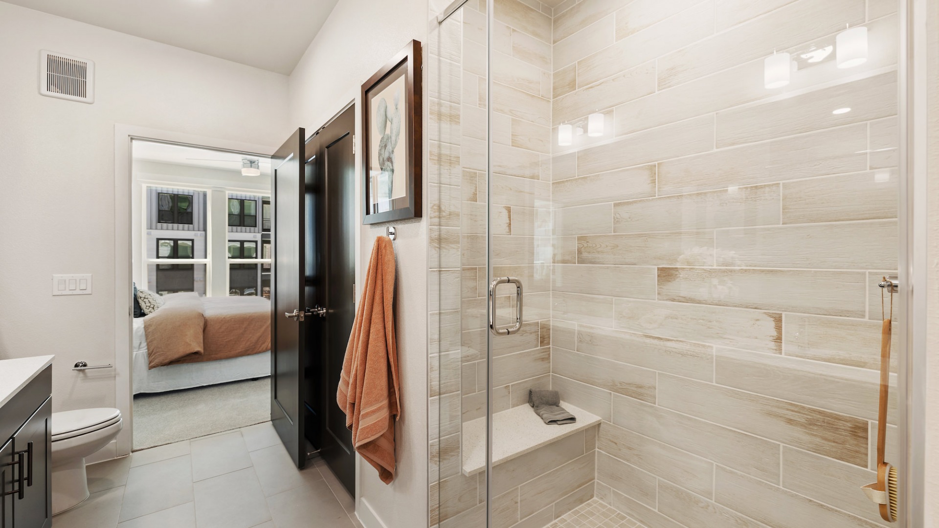 Model bathroom at our apartments in Houston, featuring a tiled shower with a glass door and a view of the bedroom.