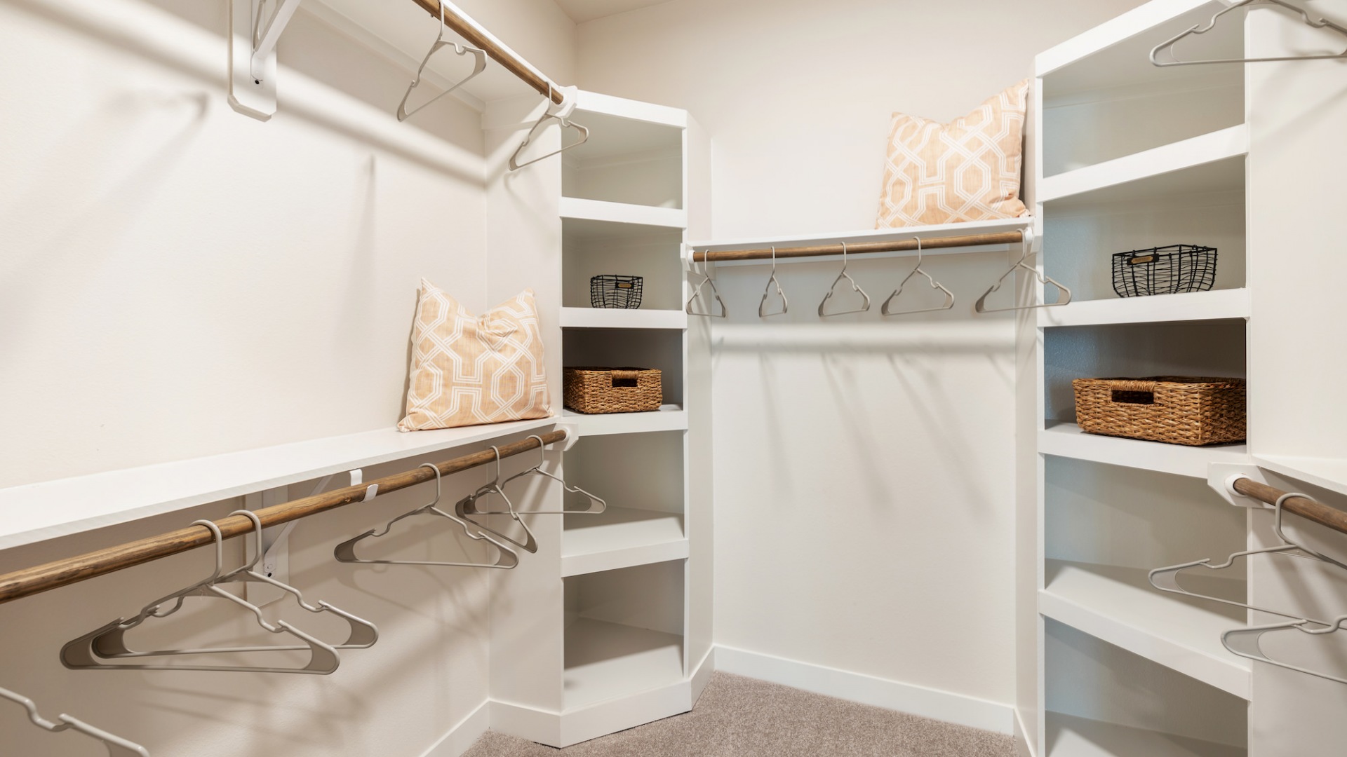 Walk in closet at our apartments in Houston, featuring clothes hangers, cubbies, and carpeted floors.